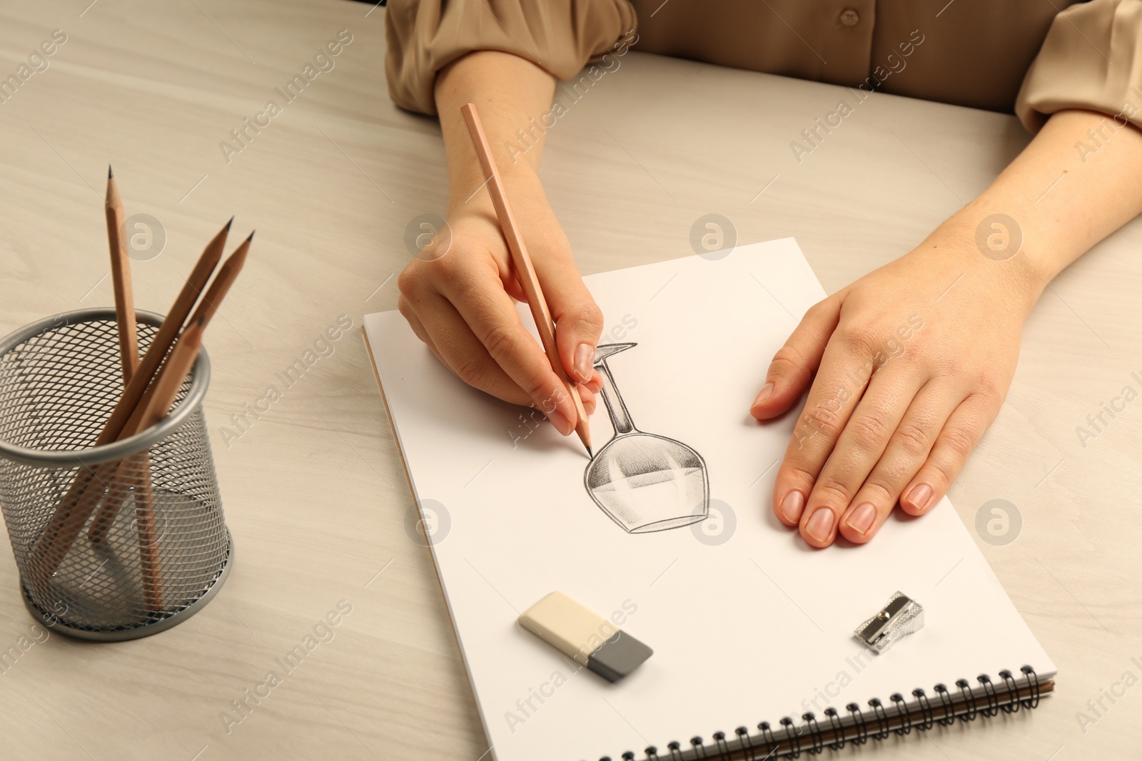 Photo of Woman drawing glass of wine with graphite pencil at light wooden table, closeup