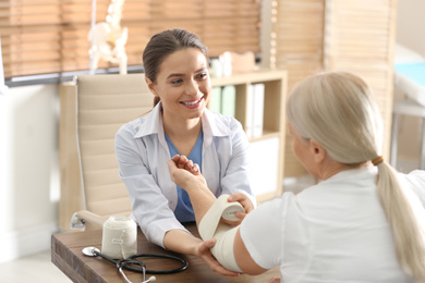 Female orthopedist applying bandage onto patient's elbow in clinic