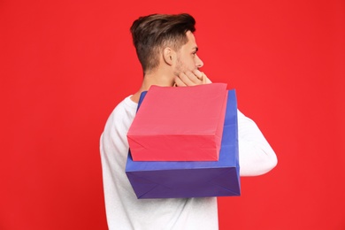 Young man with paper bags on red background