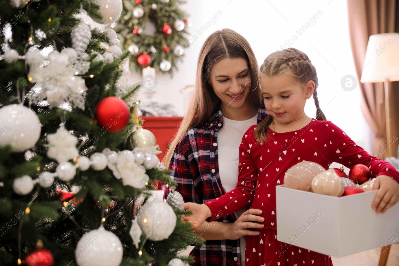 Photo of Happy mother with her cute daughter decorating Christmas tree together at home