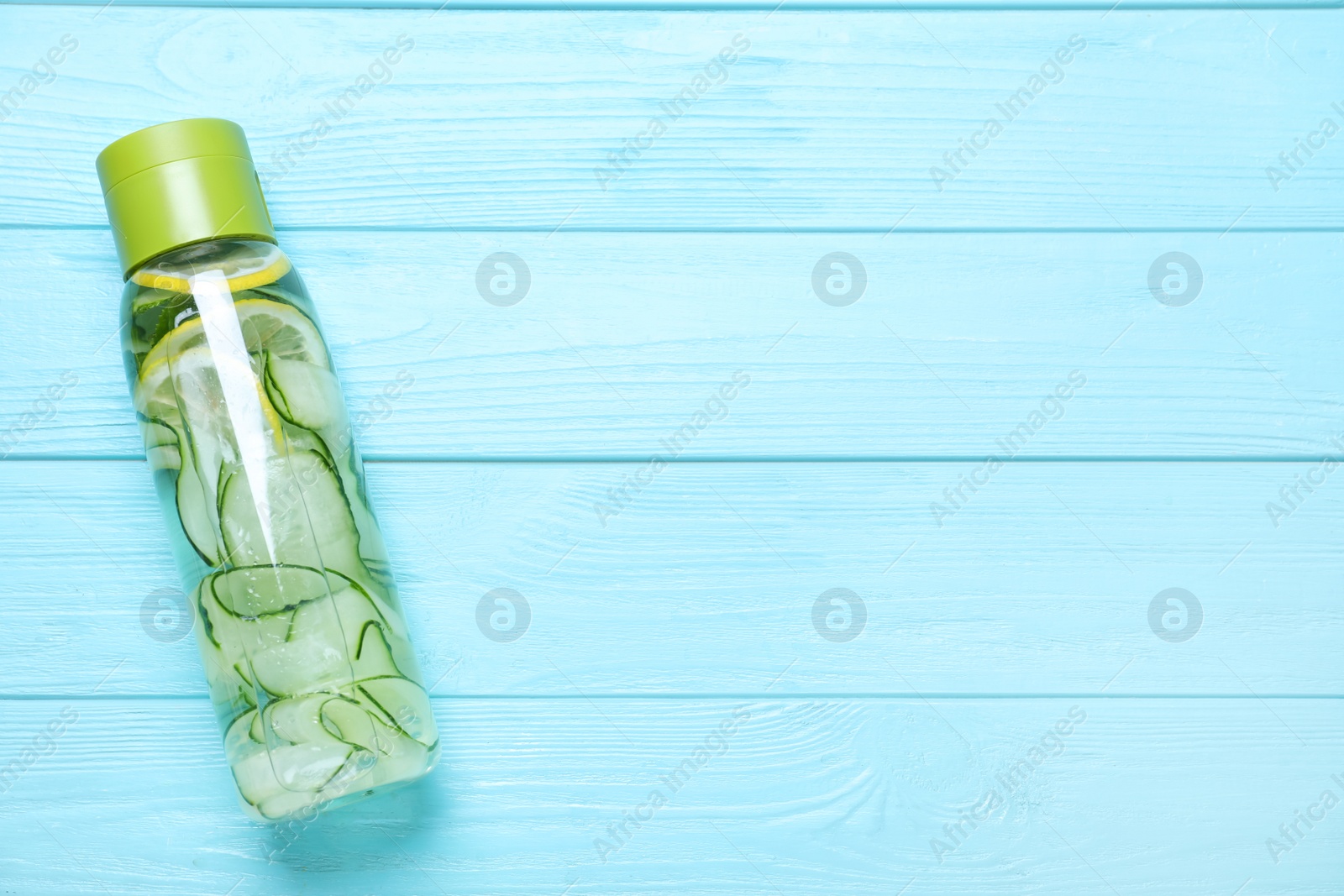 Photo of Bottle of refreshing water with cucumber, lemon and mint on light blue wooden table, top view. Space for text