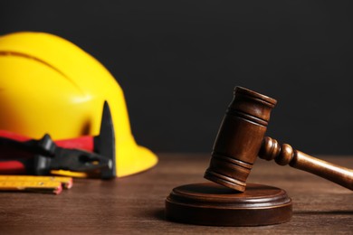 Photo of Construction and land law concepts. Gavel, hard hat and different tools on wooden table, closeup with space for text