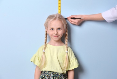 Photo of Doctor measuring little girl's height on light background