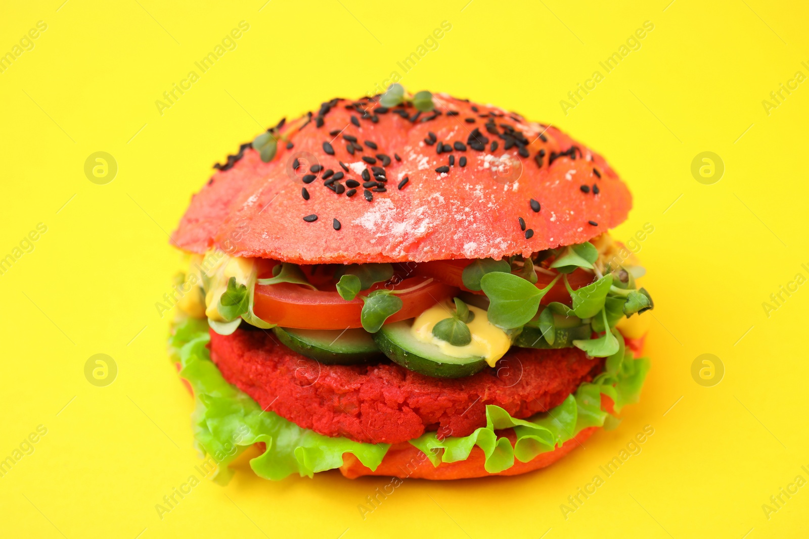 Photo of Tasty pink vegan burger with vegetables, patty and microgreens on yellow background, closeup