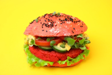 Photo of Tasty pink vegan burger with vegetables, patty and microgreens on yellow background, closeup