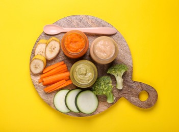 Photo of Glass jars with healthy baby food and ingredients on yellow background, top view