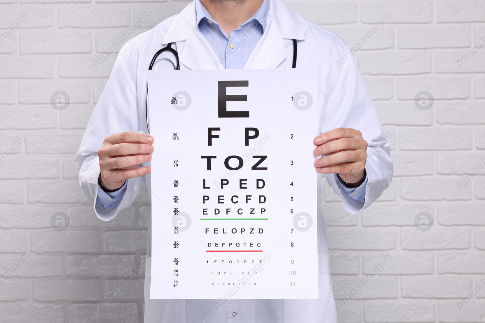 Photo of Ophthalmologist with vision test chart near white brick wall, closeup