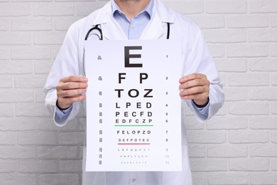 Ophthalmologist with vision test chart near white brick wall, closeup