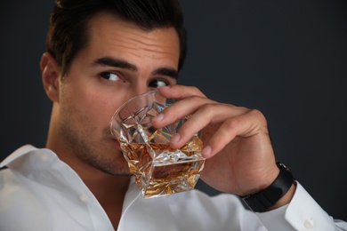 Young man with glass of whiskey on dark background