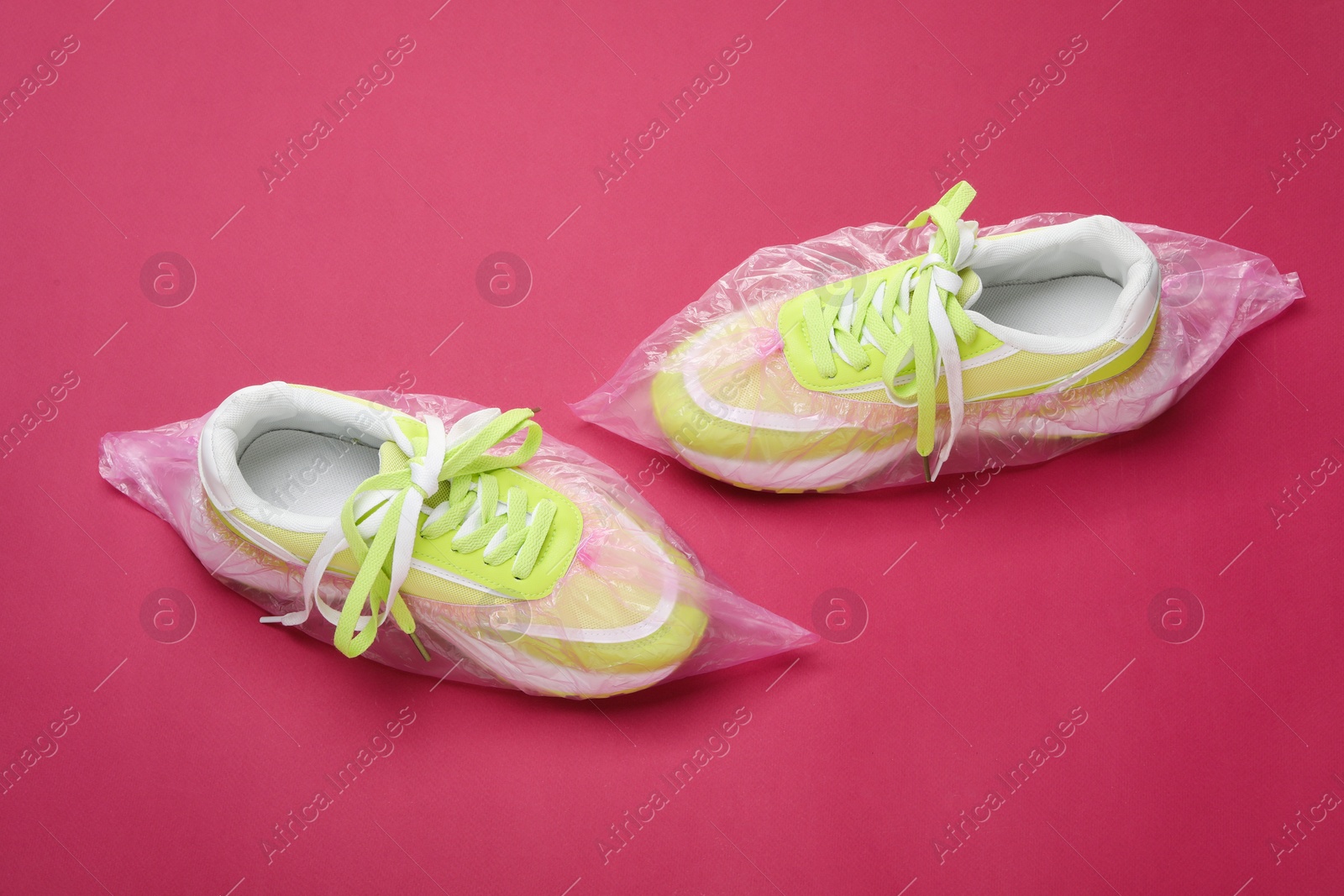 Photo of Sneakers in shoe covers on pink background, above view
