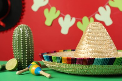 Composition with Mexican sombrero hat and maracas on green table, closeup