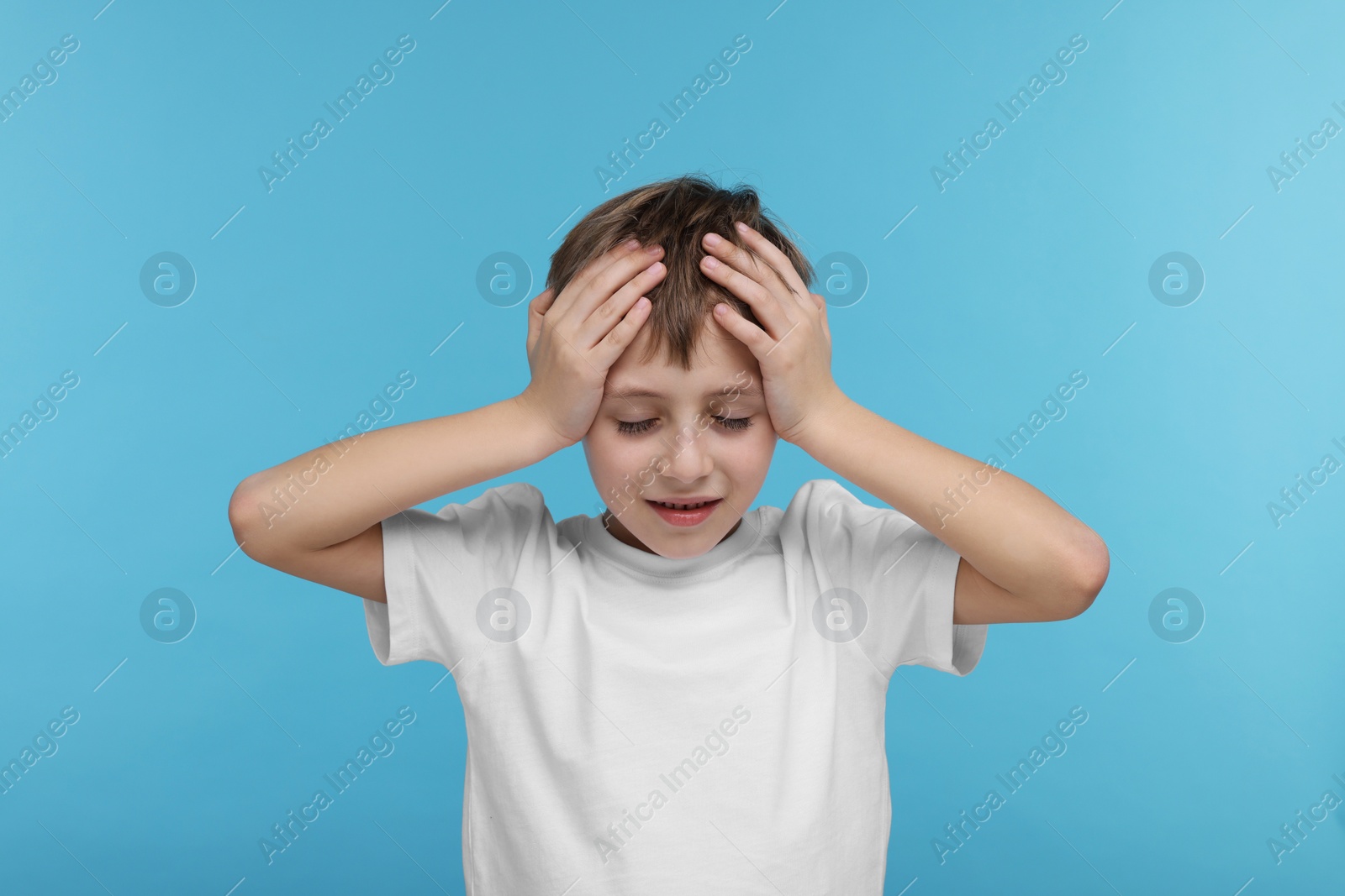 Photo of Little boy suffering from headache on light blue background