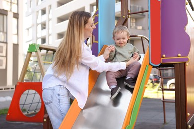 Photo of Happy nanny and cute little boy on slide outdoors
