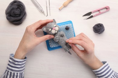 Woman felting toy cat from wool at light wooden table, top view