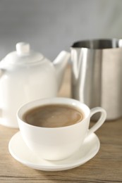 Photo of Aromatic tea with milk in cup, teapot and pitcher on wooden table,