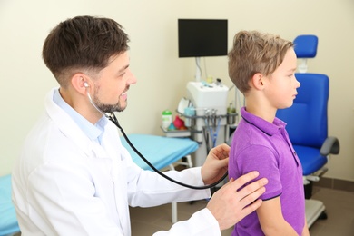 Photo of Male doctor examining little child with stethoscope in hospital