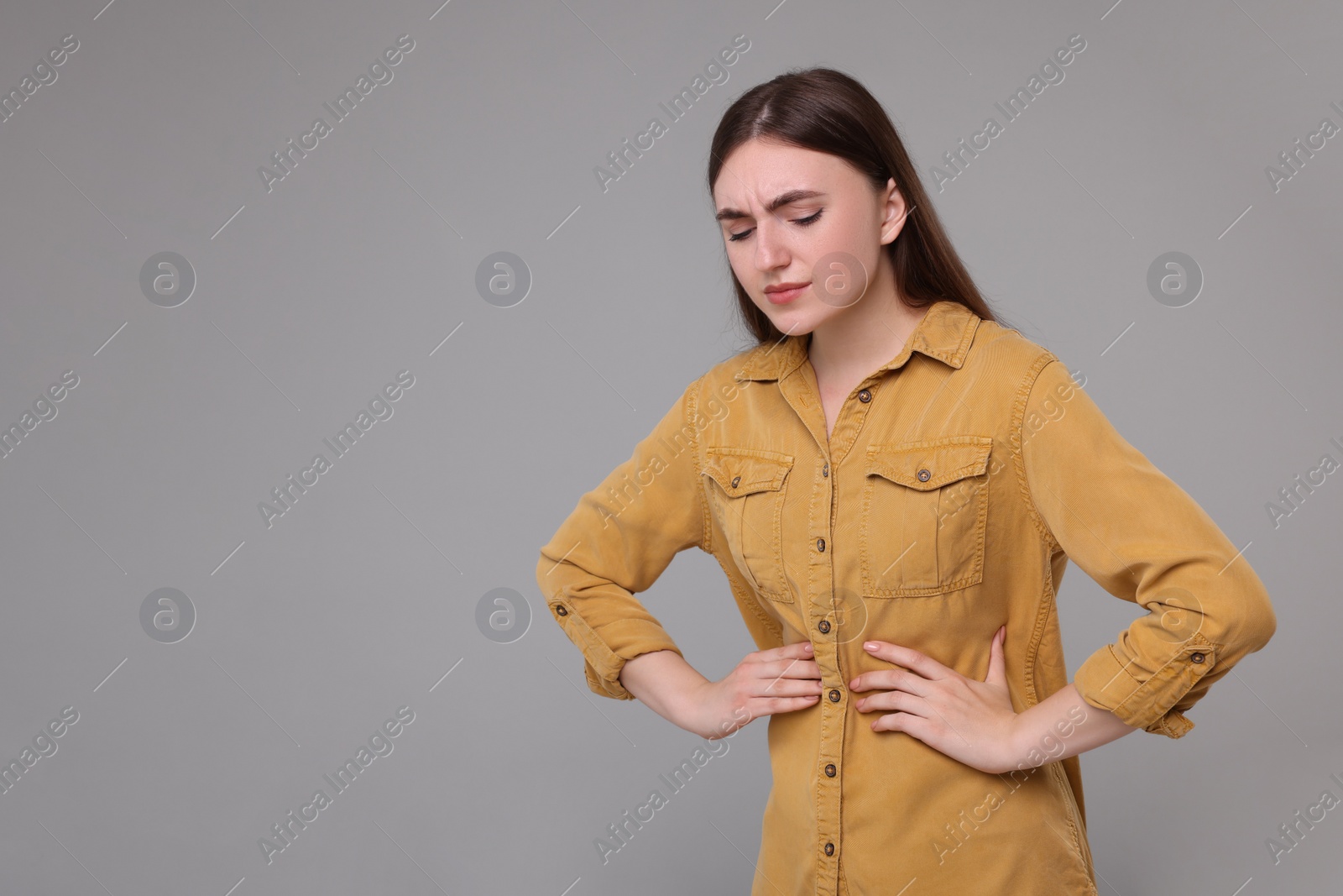 Photo of Young woman suffering from stomach pain on grey background. Space for text