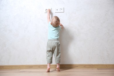 Photo of Little child playing with electrical socket indoors, back view. Dangerous situation