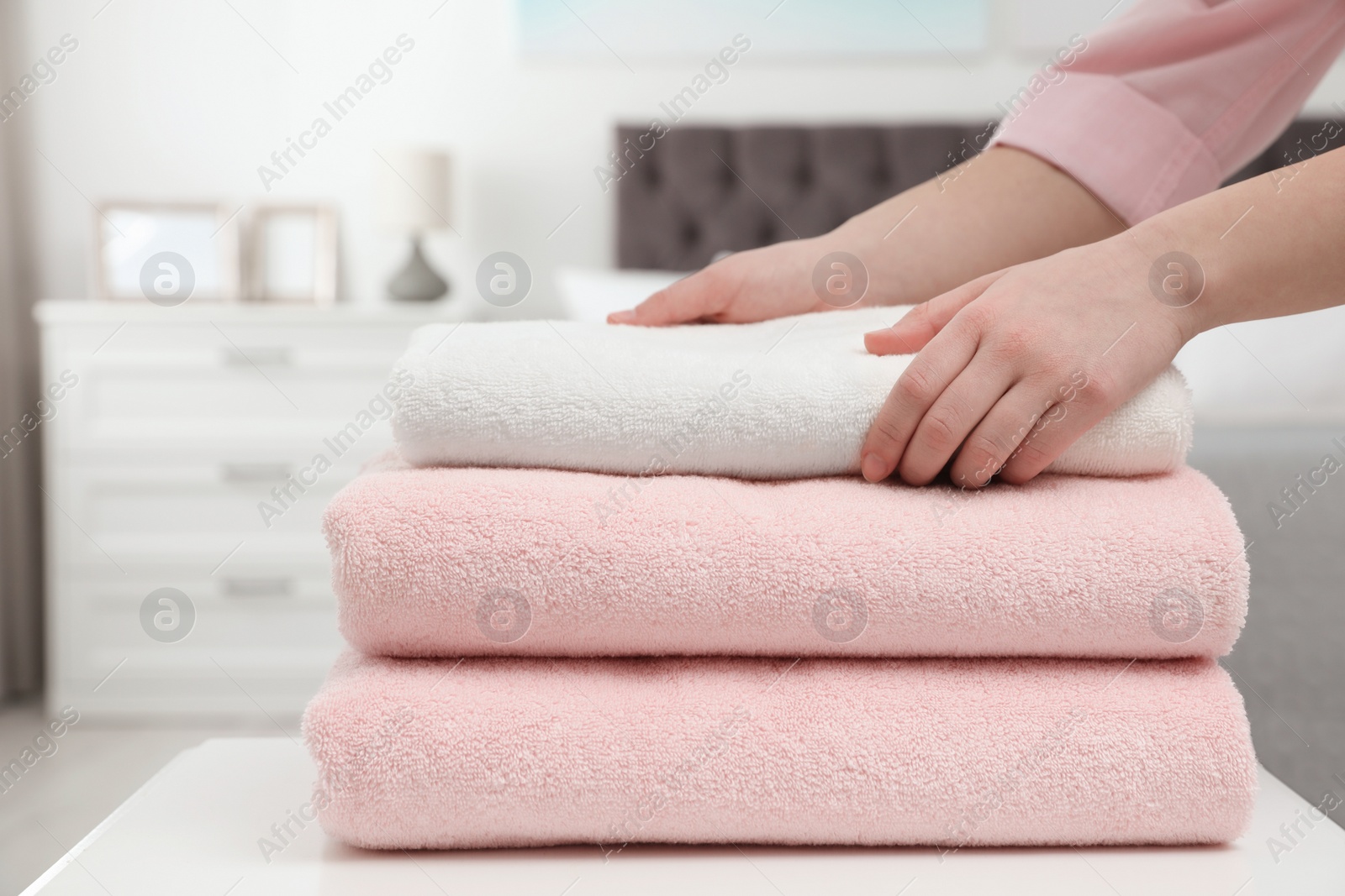 Photo of Woman stacking clean towels on table in bedroom