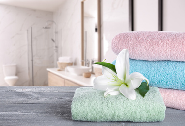 Image of Fresh towels and lily flower on grey wooden table in bathroom. Space for text