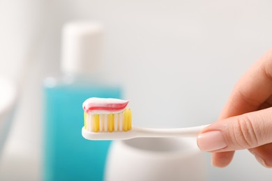 Photo of Woman holding toothbrush with paste against blurred background, closeup