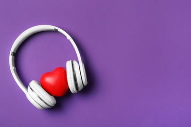 Photo of Modern headphones and red heart on purple background, flat lay with space for text. Listening love music songs