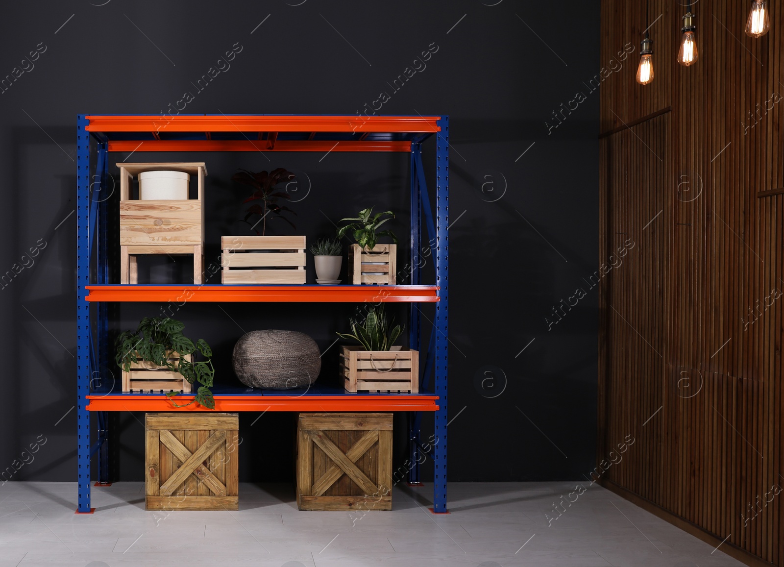 Photo of Metal shelving unit with wooden crates and different household stuff near black wall indoors