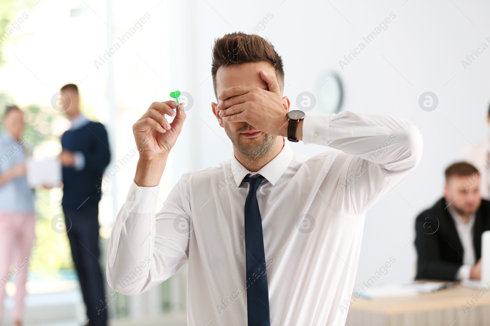 Photo of Young businessman playing darts with his eyes closed