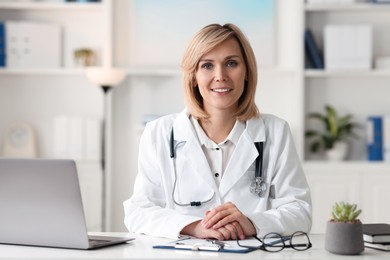 Photo of Smiling doctor with laptop having online consultation at table in office