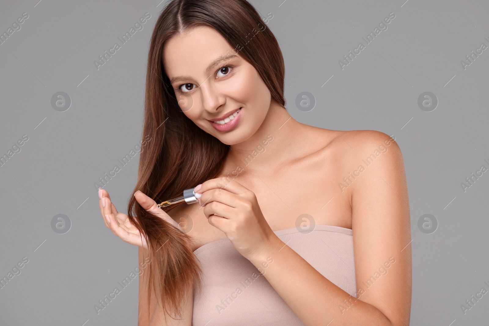 Photo of Beautiful woman applying serum onto hair on grey background