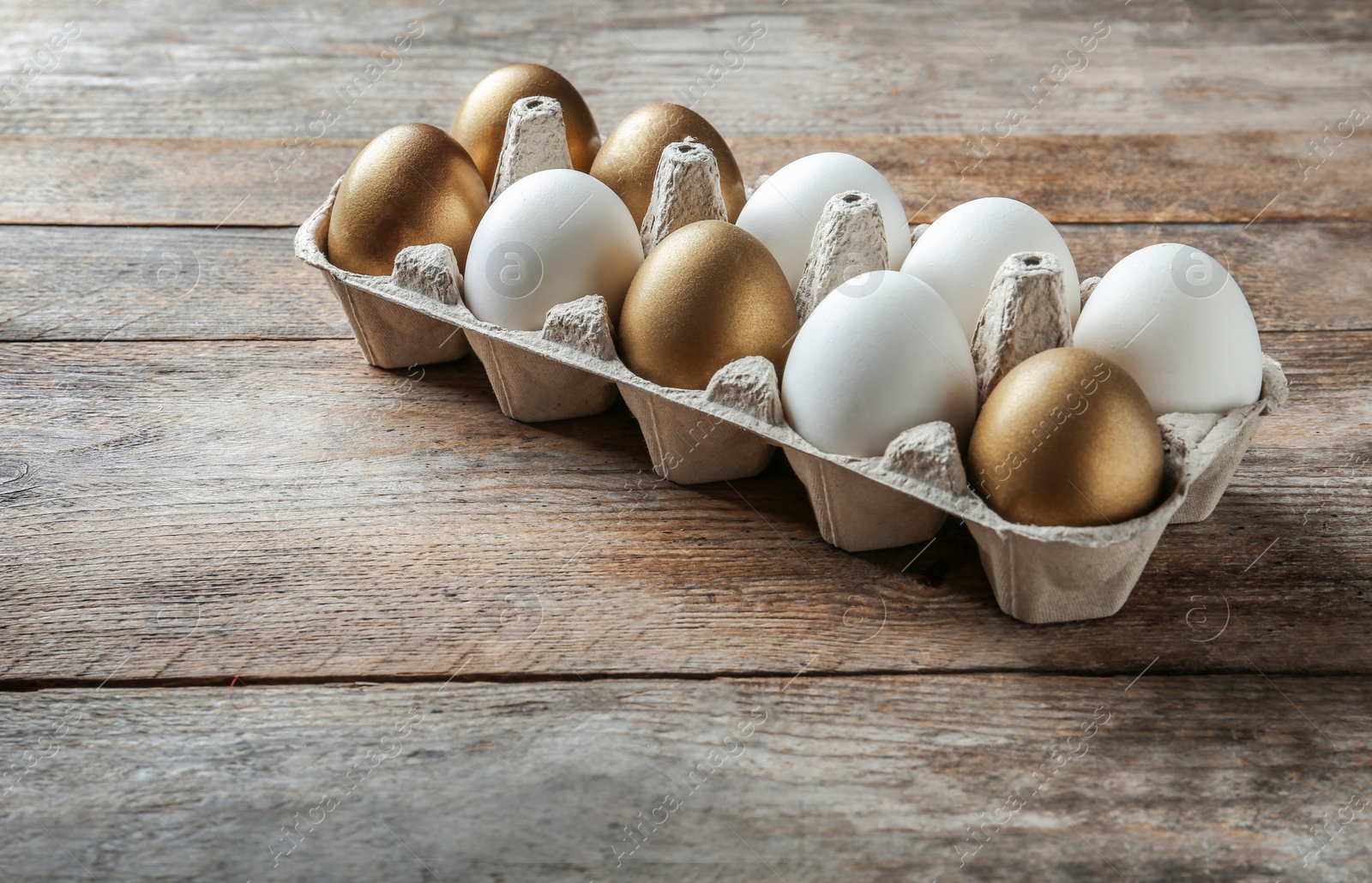 Photo of Golden eggs among others in carton on wooden background, space for text