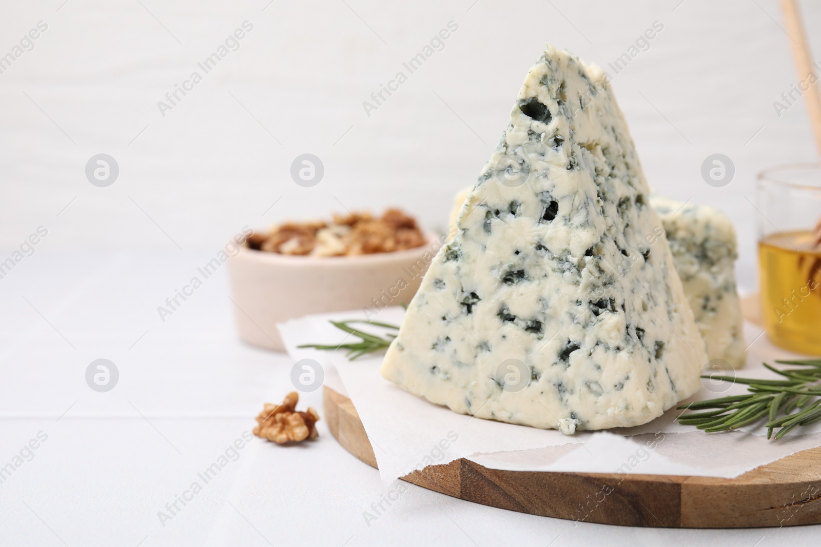 Photo of Tasty blue cheese with rosemary, honey and walnuts on white tiled table. Space for text