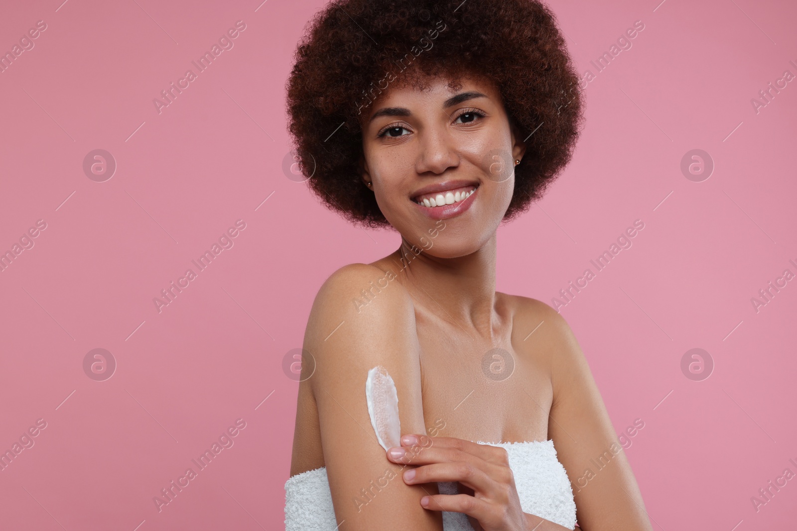 Photo of Beautiful young woman applying body cream onto arm on pink background, space for text