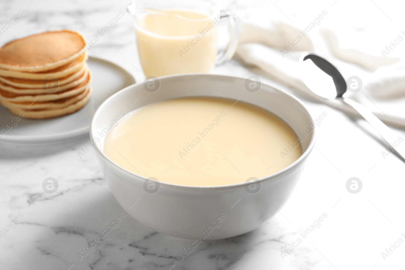 Photo of Bowl with condensed milk on marble table. Dairy products