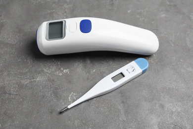 Photo of Non-contact infrared and digital thermometers on grey stone background