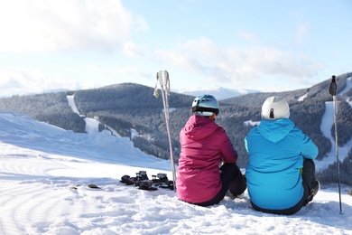 Couple with ski equipment sitting on snowy hill in mountains, space for text. Winter vacation