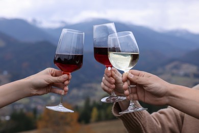 Photo of Friends clinking glasses of wine in mountains, closeup
