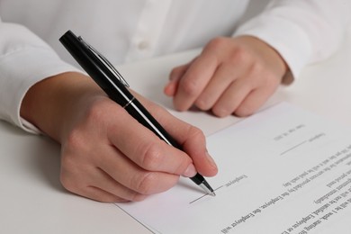 Photo of Businesswoman signing contract at white table, closeup of hands