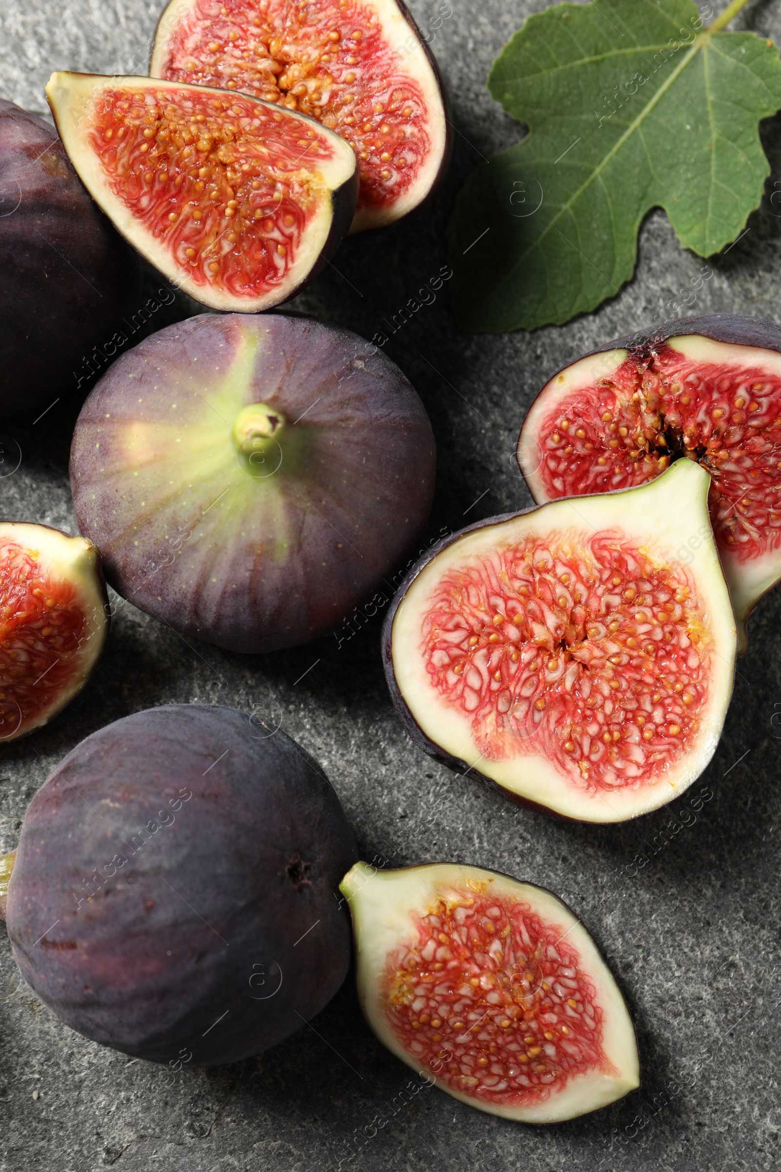 Photo of Whole and cut ripe figs with leaf on grey textured table, flat lay