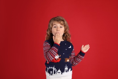Photo of Little girl in Christmas sweater covering her mouth against red background