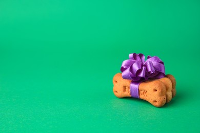 Photo of Bone shaped dog cookies with purple bow on green background. Space for text