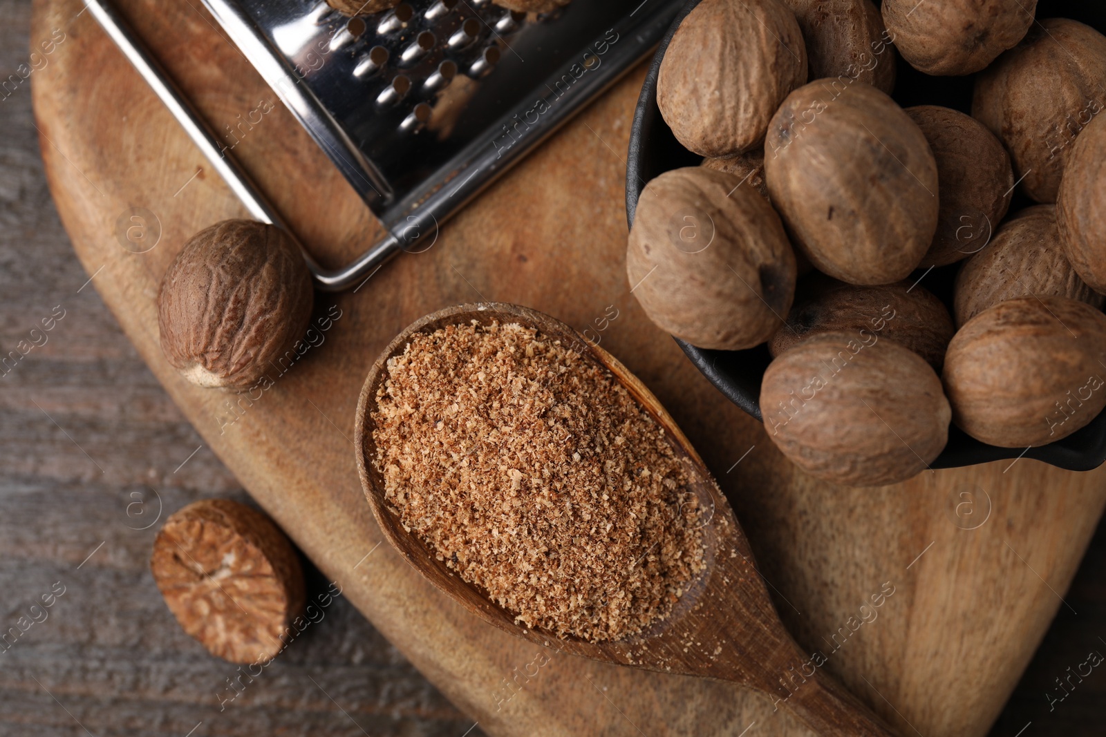 Photo of Spoon with grated nutmeg, seeds and grater on wooden table, top view