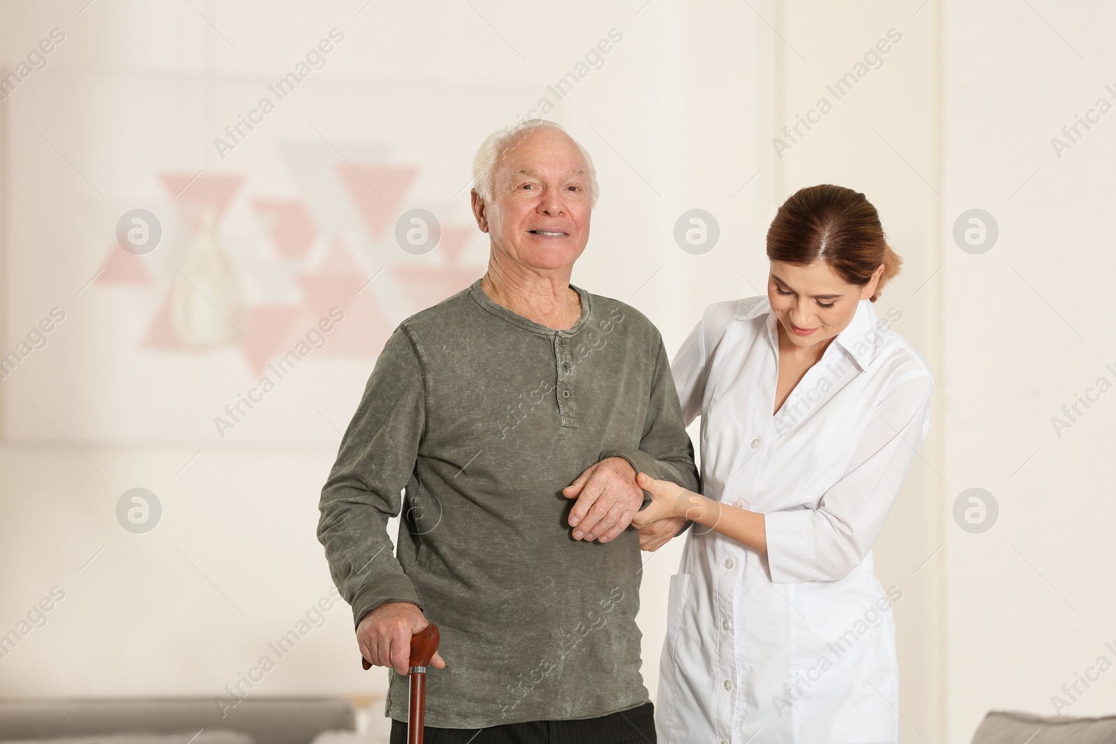 Photo of Elderly man with walking cane and female caregiver in room