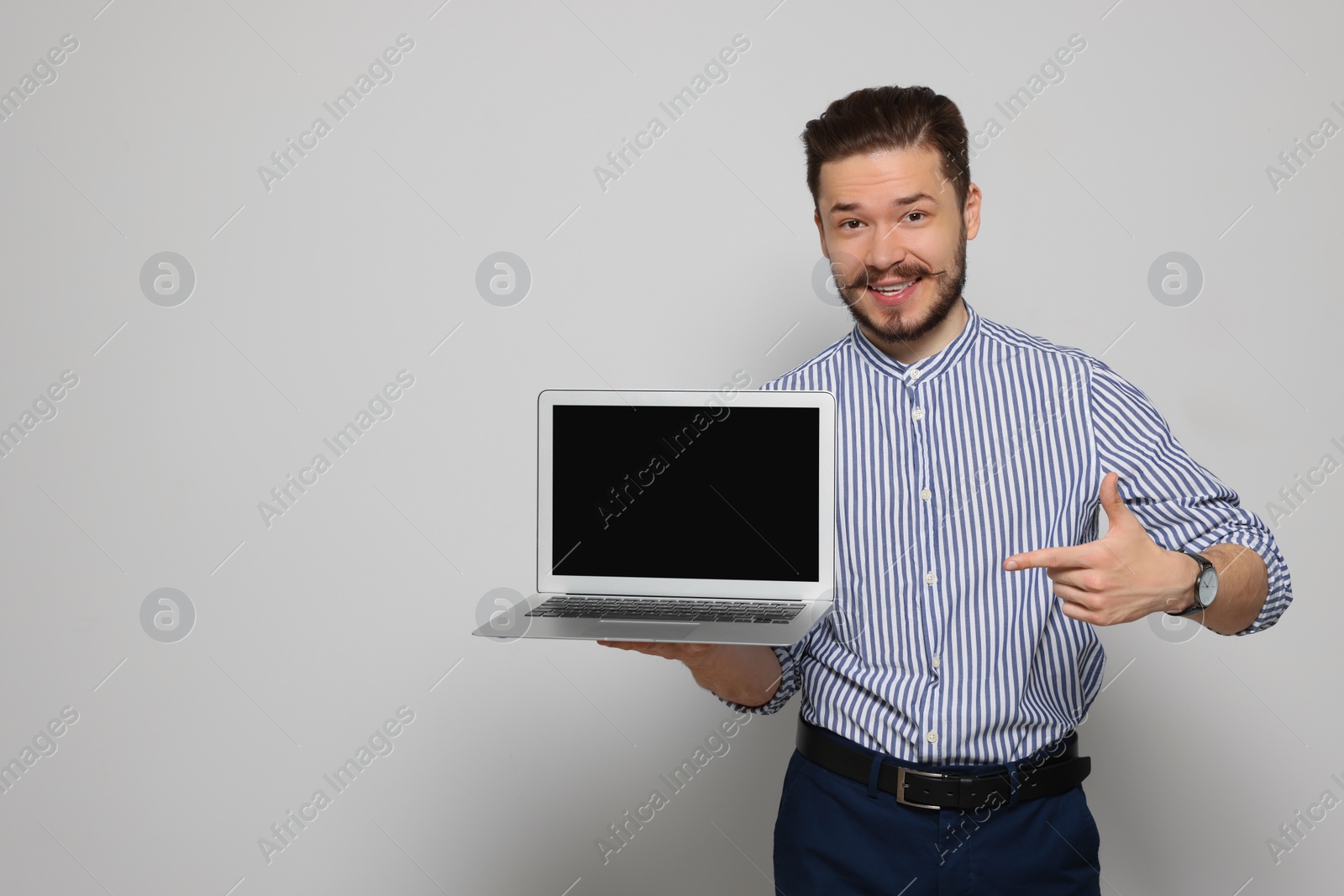 Photo of Emotional man pointing at laptop on light grey background. Space for text