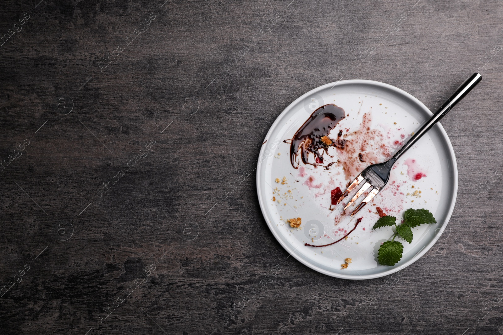 Photo of Dirty plate with food leftovers, mint and fork on grey background, top view. Space for text