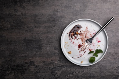 Photo of Dirty plate with food leftovers, mint and fork on grey background, top view. Space for text