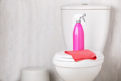 Photo of Spray bottle and rag on toilet bowl indoors. Cleaning supplies