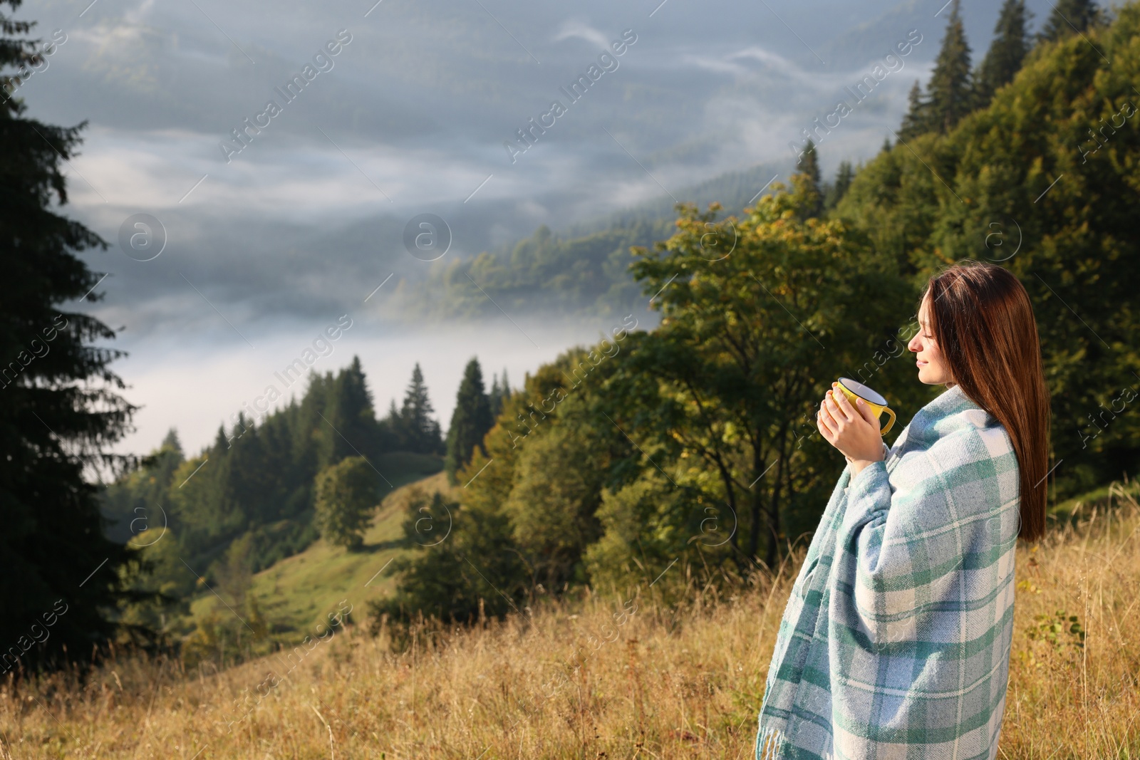 Photo of Woman with cozy plaid enjoying cup of hot beverage in nature