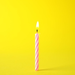 Photo of Burning pink striped birthday candle on yellow background