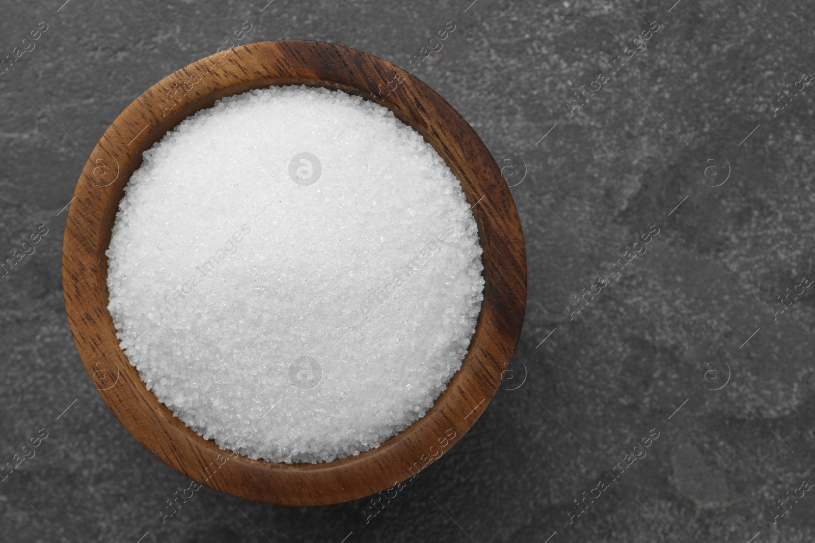 Photo of Granulated sugar in bowl on grey textured table, top view. Space for text